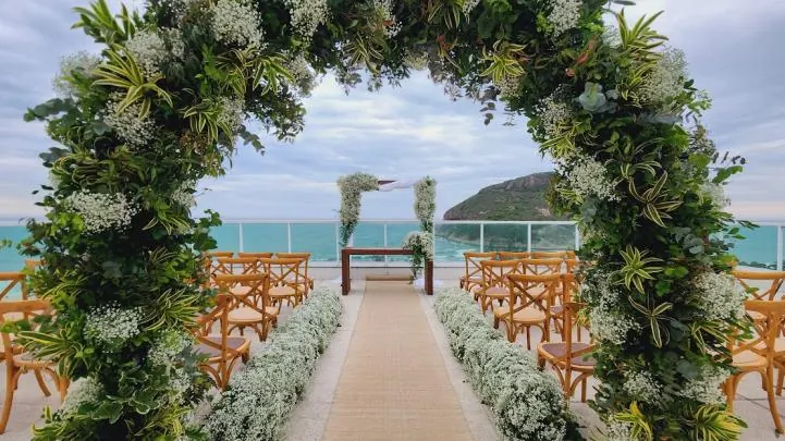 Arco de folhagens e flores brancas sobre a nave, com o mar ao fundo